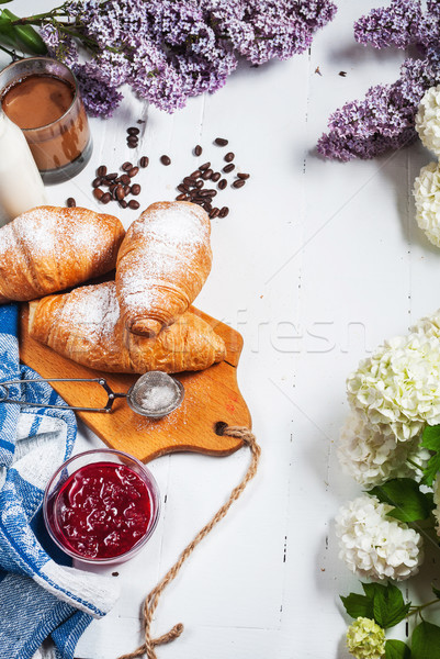 Breakfast with fresh croissants, glass of coffee, milk, strawberry jam and flowers on a white wooden Stock photo © voloshin311