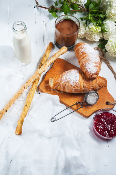 Breakfast with fresh croissants, glass of coffee, milk, strawberry jam and flowers on a white wooden Stock photo © voloshin311
