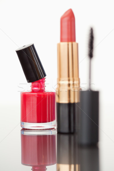 Stock photo: A mascara tube with a pale red lipstick and a red nail polish flask against a white background