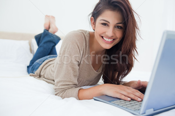 Сток-фото: улыбающаяся · женщина · ног · ноутбука · кровать · рук