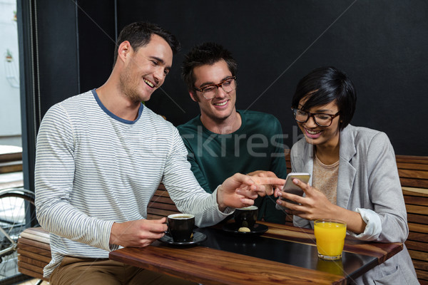 Friends drinking coffee and orange juice while looking at smartp Stock photo © wavebreak_media