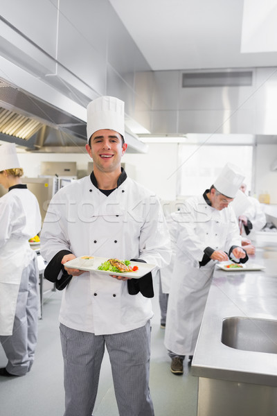 Happy chef holding a salmon dish in busy kitchen Stock photo © wavebreak_media