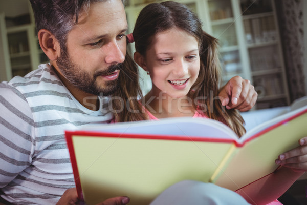 Stock photo: Smiling father and daughter looking at photo album in living room