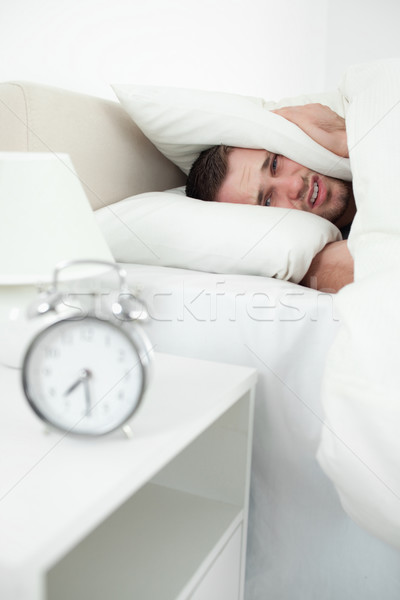 Portrait of an attractive man covering his ears with a pillow while his alarm clock is ringing Stock photo © wavebreak_media