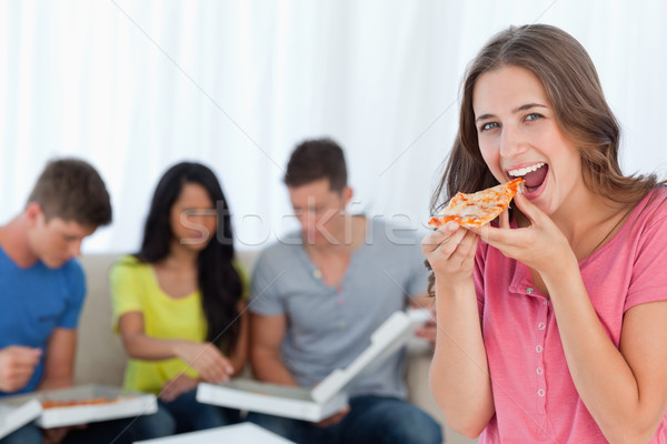 A smiling woman in front of her friends looks at the camera as she eats a piece of pizza Stock photo © wavebreak_media