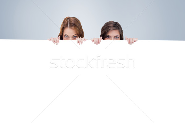 Composite image of two friends secretly hiding behind a blank po Stock photo © wavebreak_media