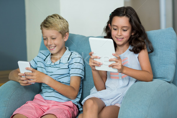 Siblings using digital tablet and mobile phone in living room Stock photo © wavebreak_media