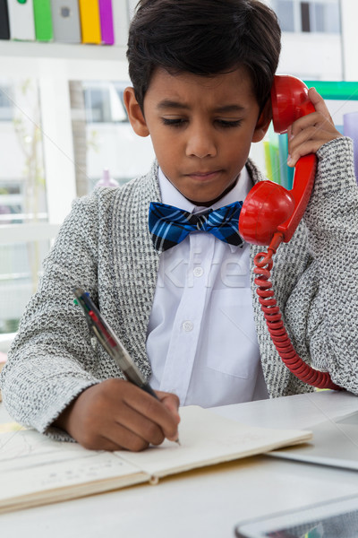 Stock photo: Boy imitating as businessman writing on book while using landline