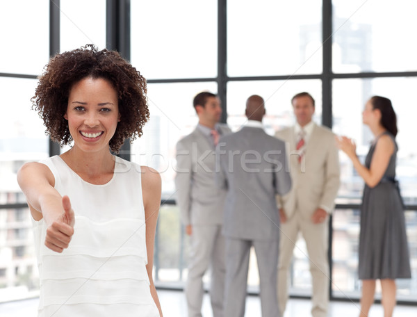 Stock photo: Bright Businesswoman doing a thum-up with his colleagues in the background