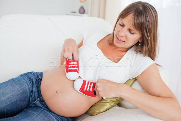 Beautiful pregnant woman playing with red baby shoes while lying on a sofa in her living room Stock photo © wavebreak_media