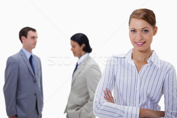 Stock photo: Businesswoman with arms folded and talking colleagues behind her against a white background