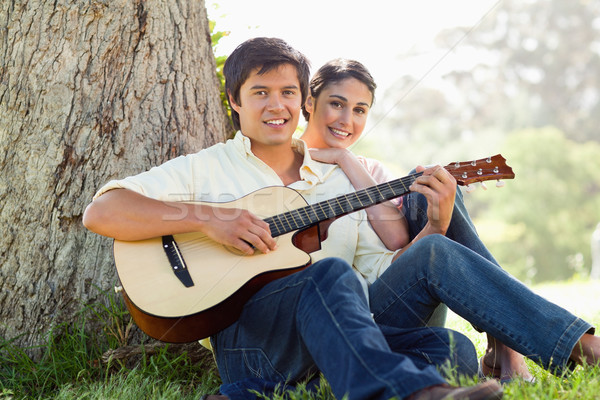 Man and his friend look straight ahead as they listen to him playing the guitar while sitting agains Stock photo © wavebreak_media