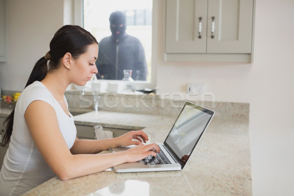 Woman using a laptop in the kitchen with burglar standing at the window Stock photo © wavebreak_media