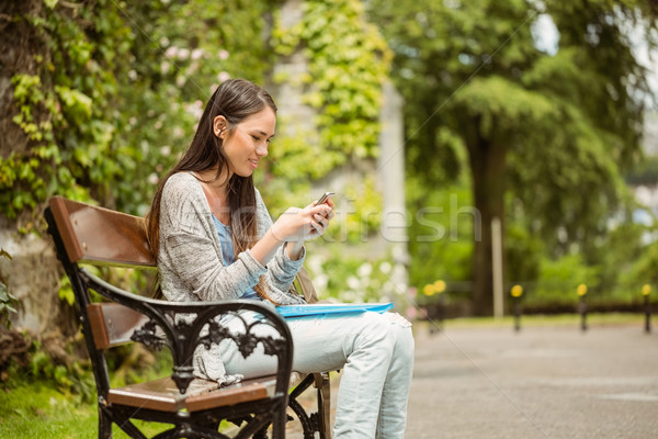 Smiling student sitting on bench text message on her mobile phon Stock photo © wavebreak_media