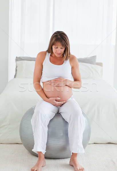 Lovely pregnant female caressing her belly while sitting on a gym ball in her bedroom Stock photo © wavebreak_media