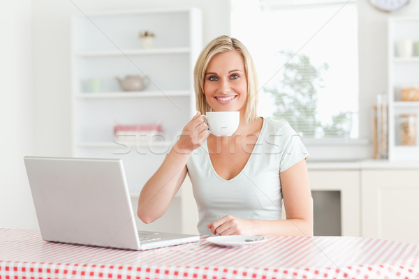 Woman drinking coffee with laptop in front of her looking into the camera in the kitchen Stock photo © wavebreak_media