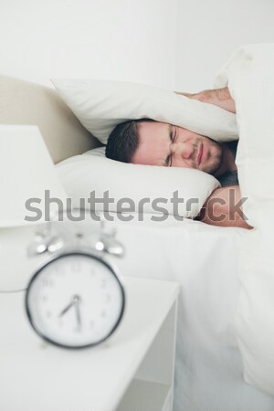 Exhausted woman covering her ears with a duvet while her alarm clock is ringing Stock photo © wavebreak_media