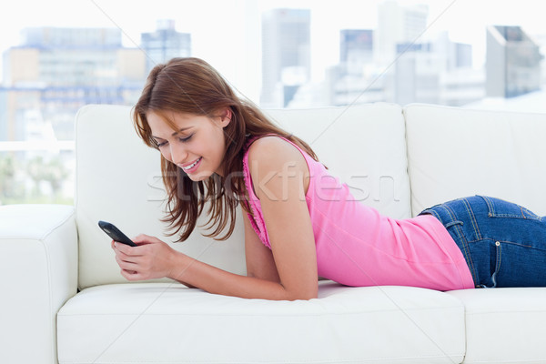 Young smiling woman sending a text and lying on a comfy sofa Stock photo © wavebreak_media