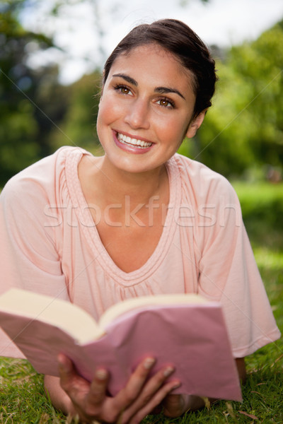 Woman looks towards to the sky while she reads a books as she is lying prone on grass Stock photo © wavebreak_media