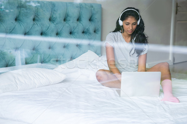 Stock photo: Woman listening to music while using laptop