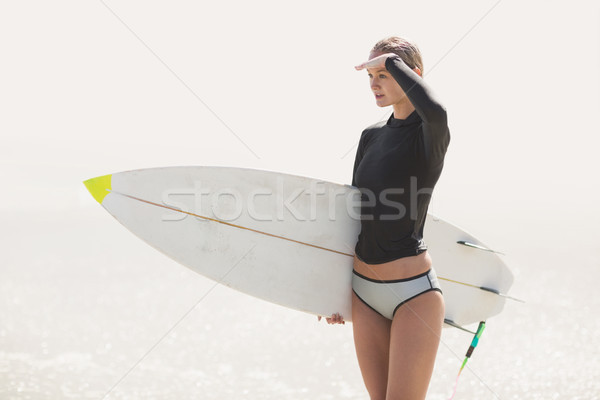 Woman with surfboard shielding eyes at beach Stock photo © wavebreak_media