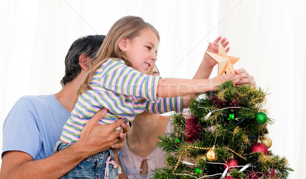 Little girl placing a star in a Christmas tree with her parents Stock photo © wavebreak_media