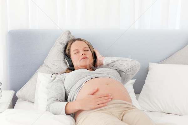 Stock photo: Relaxed future mom listening to the music on a bed at home