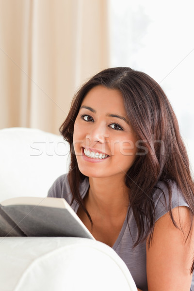 close up of a dark-haired woman lying on sofa reading a book looking into camera in livingroom Stock photo © wavebreak_media