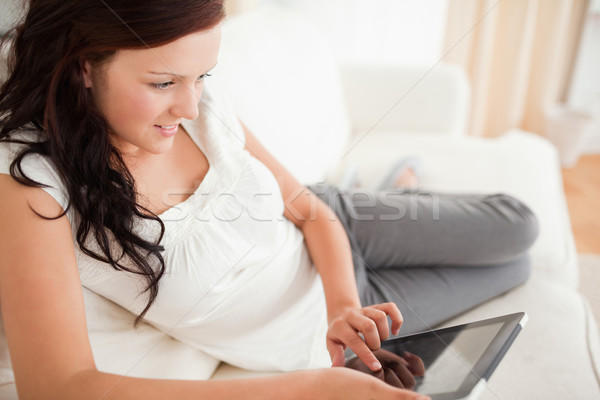 Beautiful red-haired woman lying on a sofa with a tablet in the livingroom Stock photo © wavebreak_media