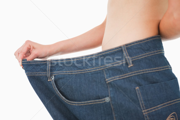 Stock photo: Close-up of a woman belly in a too big pants against white background