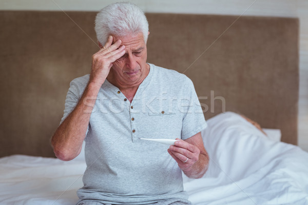 Senior om termometru şedinţei pat casă Imagine de stoc © wavebreak_media