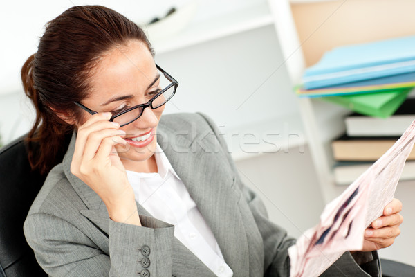 Cheerful businesswoman holding her glasses and reading a newspaper in her office sitting at her desk Stock photo © wavebreak_media