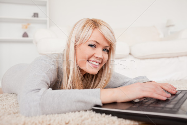 Stock photo: Beautiful blond woman relaxing on laptop lying on a carpet in the living room
