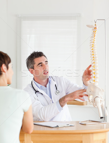 Stock photo: Doctor showing a female patient a part of a spine in a room