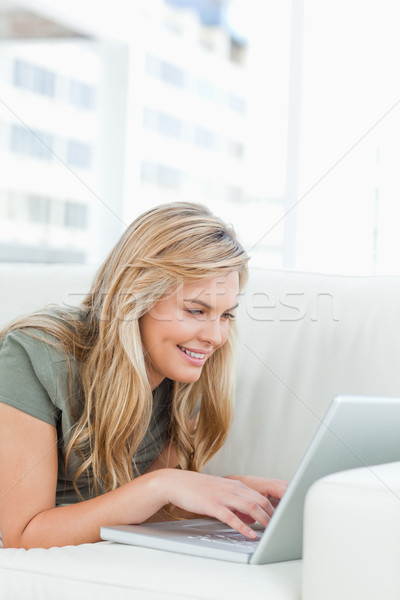 A woman smiling as she uses her laptop and lying across the couch. Stock photo © wavebreak_media