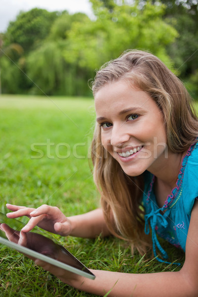 Smiling teenager lying down on the grass in a parkland while touching her tablet pc Stock photo © wavebreak_media