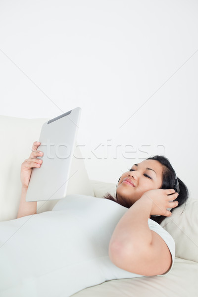 Woman lying on a couch with headphones on and holding a tactile tablet in a living room Stock photo © wavebreak_media