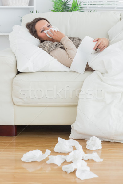 Stock photo: Sad and sick women lying on the sofa in the living room surrounded by tissues