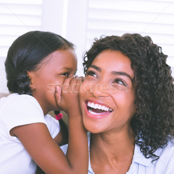 Stock photo: Pretty mother sitting on the couch with her daughter whispering 