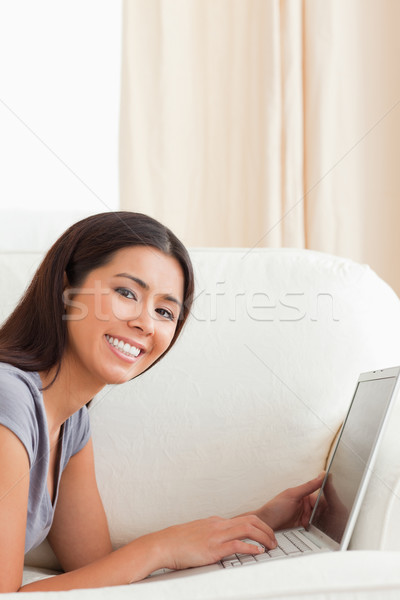 close up of a smiling woman lying on sofa with notebook looking into camera in livingroom Stock photo © wavebreak_media