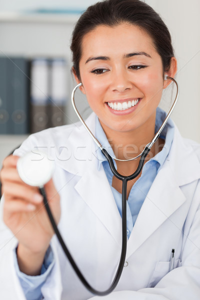 Stock photo: Pretty female doctor using a stethoscope while looking at the camera in her office