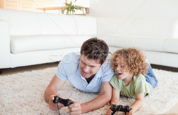 Cheerful boy and his father playing video games while lying on a carpet Stock photo © wavebreak_media