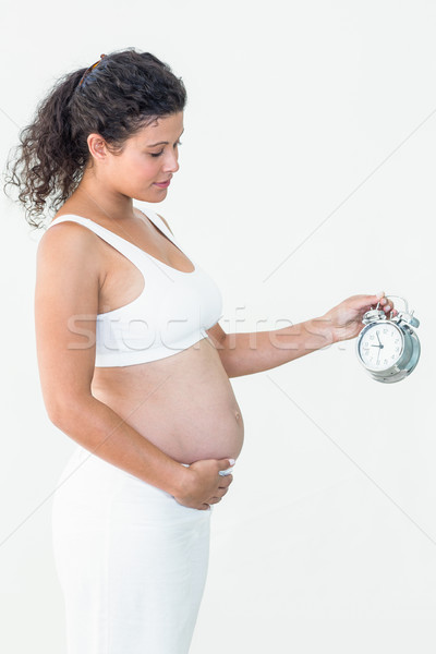 Foto stock: Mulher · grávida · olhando · despertador · tocante · barriga · branco