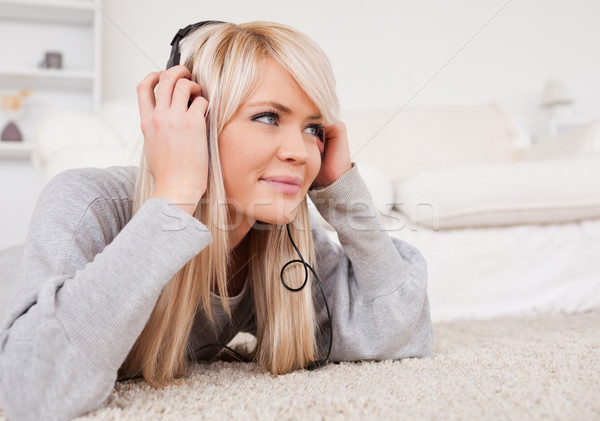 Stock photo: Beautiful blond woman with headphones lying on a carpet in the living room