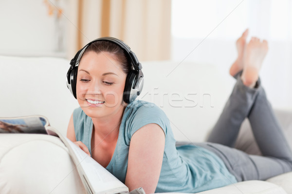 Stock photo: Lovely woman with headphones reading a magazine while lying on a sofa in the living room