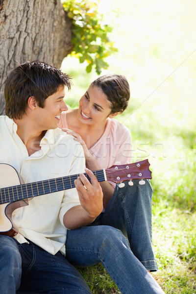 Smiling woman looking eye to eye with her friend who is holding a guitar as they both sit against a  Stock photo © wavebreak_media