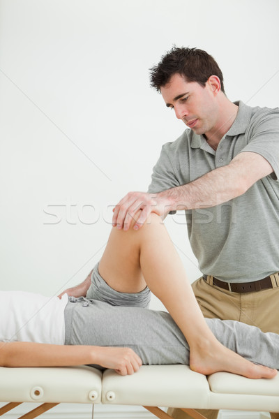 Stock photo: Serious physiotherapist stretching a leg while standing in a room
