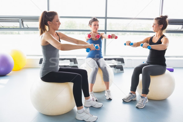 Stock photo: Three women lifting weights together on exercise balls in gym