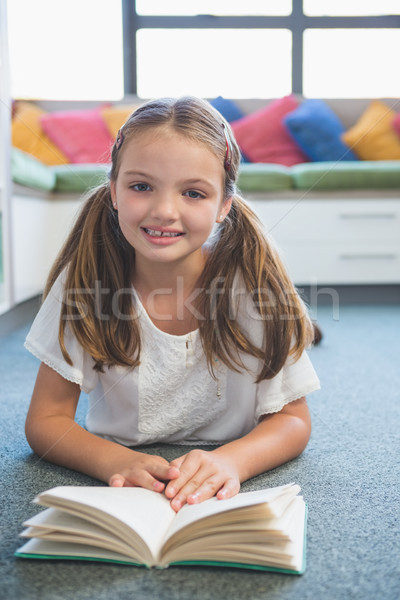 Schoolgirl lying on floor and reading a book in library Stock photo © wavebreak_media