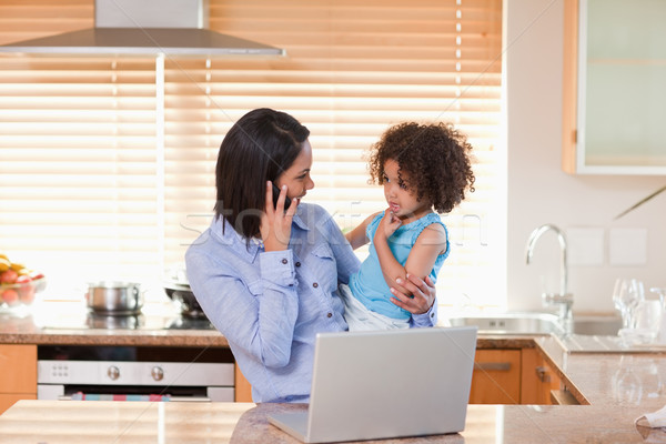 Young mother and daughter with cellphone and notebook in the kitchen together Stock photo © wavebreak_media